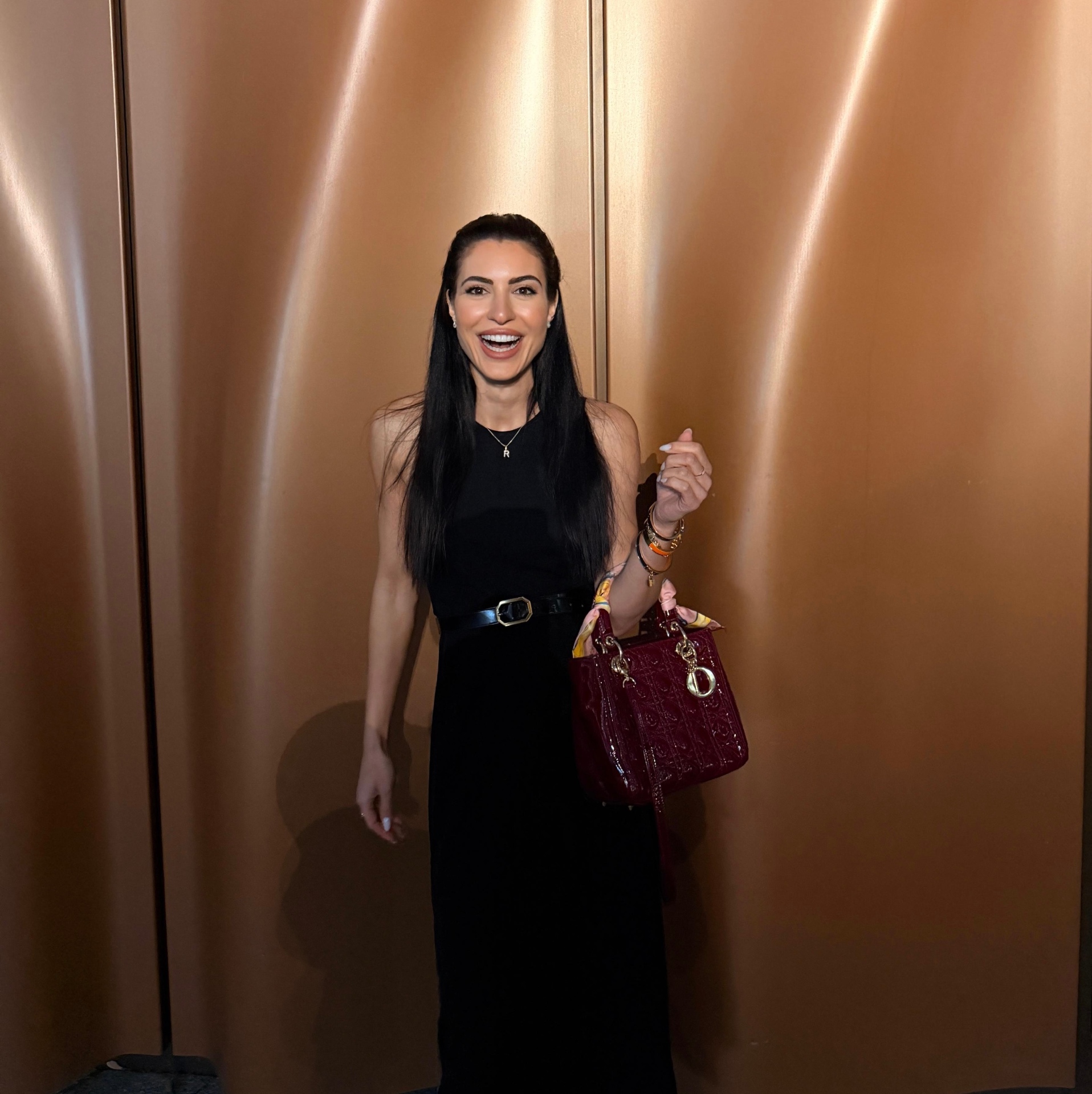 Romana Holly in an elegant black dress against a warm bronze backdrop